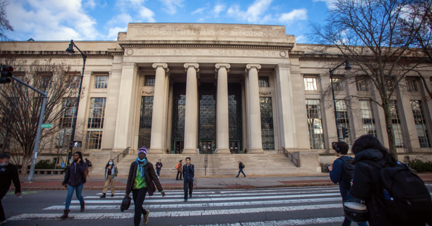 Students walking across the crosswalk, with MIT Building 7 in the background.